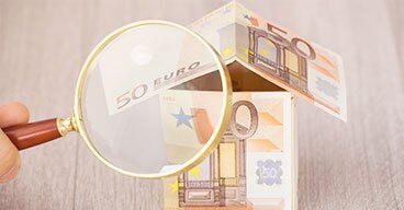 Haus aus 50 Euro Scheinen unter einer Lupe